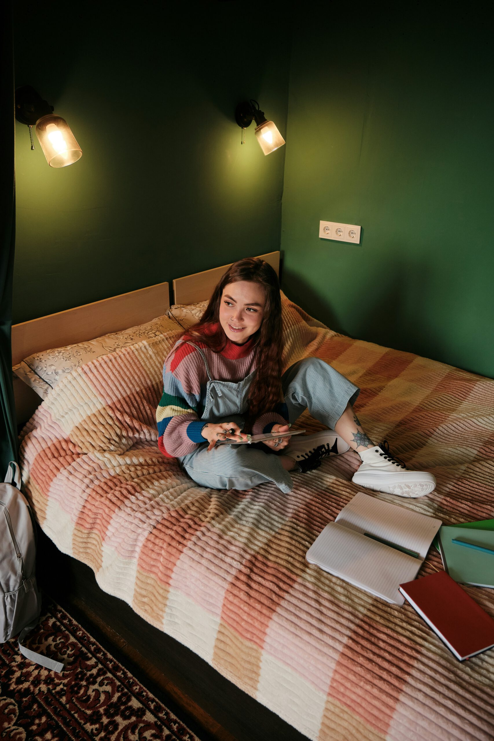 Student sitter med ipad på säng i grönt sovrum